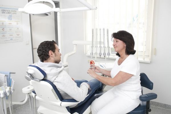 zahnarztpraxis mit patient am stuhl dem gerade das gebiss erklärt wird